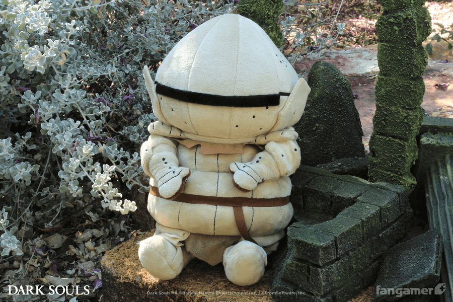 The Siegmeyer plush photographed outdoors, seated next to a flowering bush and miniature ruins.  - Siegmeyer Plush - DARK SOULS